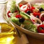 yellow olive oil in a glass dispenser with a bowl of salad of lettuce, cucumbers, black olives, red onions, tomato